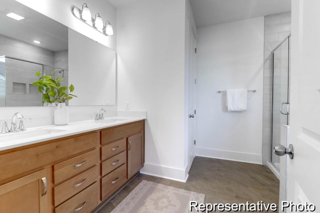 bathroom featuring a sink, baseboards, double vanity, and a shower stall