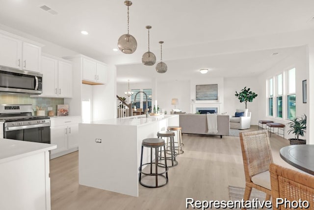 kitchen with tasteful backsplash, open floor plan, light wood-style flooring, a fireplace, and stainless steel appliances