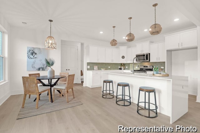 kitchen featuring light wood-style flooring, light countertops, white cabinets, appliances with stainless steel finishes, and backsplash