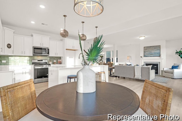 dining space featuring recessed lighting, visible vents, a glass covered fireplace, and light wood finished floors