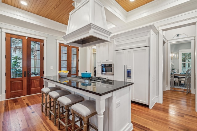 kitchen with appliances with stainless steel finishes, a kitchen breakfast bar, white cabinetry, light hardwood / wood-style floors, and french doors