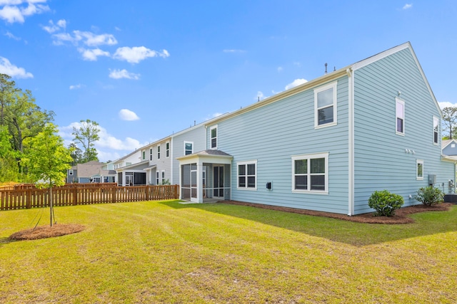 rear view of property with a lawn, a sunroom, and fence