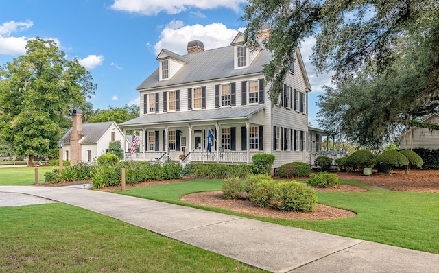 colonial house with metal roof, a chimney, a front yard, and covered porch