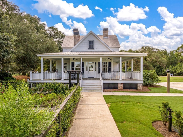 farmhouse inspired home with a chimney, a front lawn, covered porch, metal roof, and ceiling fan