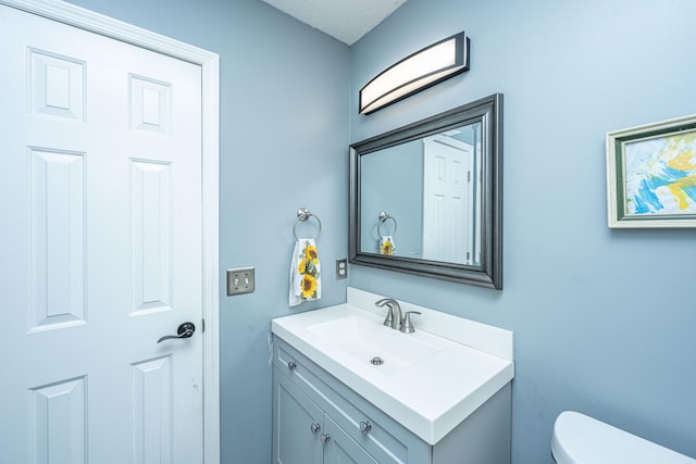 bathroom with a textured ceiling, vanity, and toilet