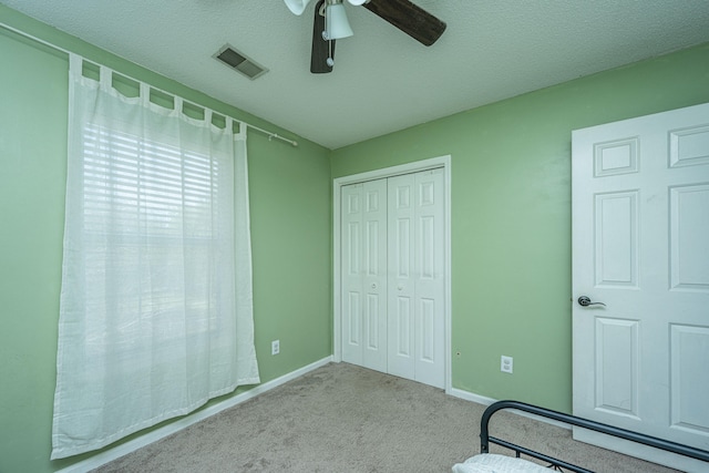 unfurnished bedroom with a closet, a textured ceiling, light colored carpet, and ceiling fan