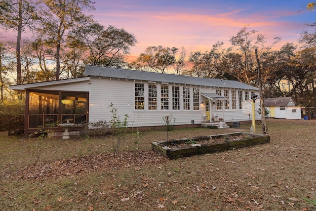 back house at dusk with a sunroom and a yard