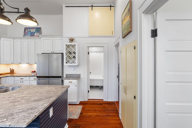 kitchen with sink, dark wood-type flooring, stainless steel fridge, white cabinetry, and light stone counters