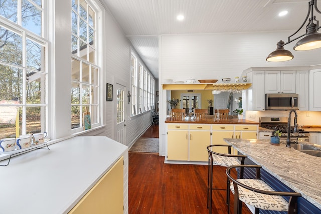 kitchen featuring dark hardwood / wood-style floors, pendant lighting, white cabinetry, sink, and light stone countertops