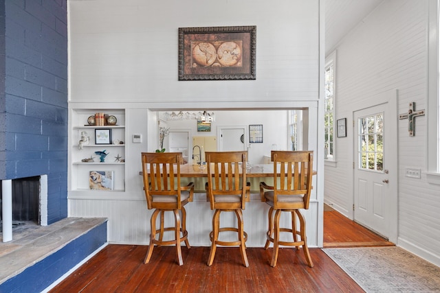 dining room featuring dark wood-type flooring, a fireplace, built in features, and a high ceiling