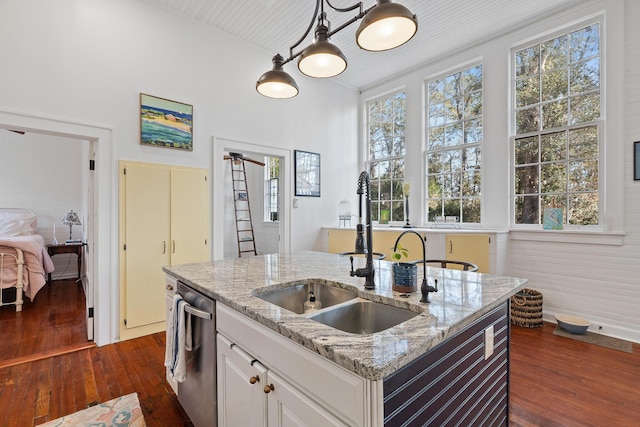 kitchen with pendant lighting, white cabinetry, sink, stainless steel dishwasher, and a center island with sink