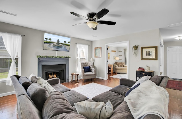 living room featuring a warm lit fireplace, a ceiling fan, baseboards, and wood finished floors