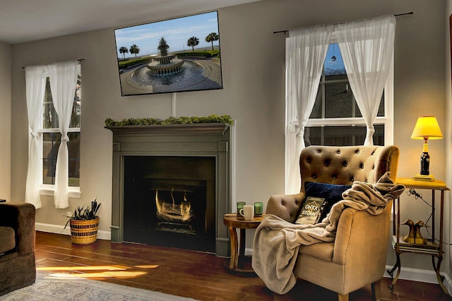 sitting room featuring a warm lit fireplace, wood finished floors, and baseboards