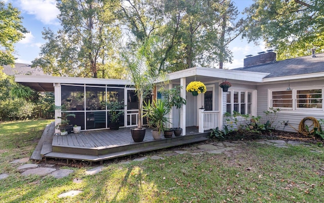 rear view of house featuring a wooden deck, a lawn, and a sunroom