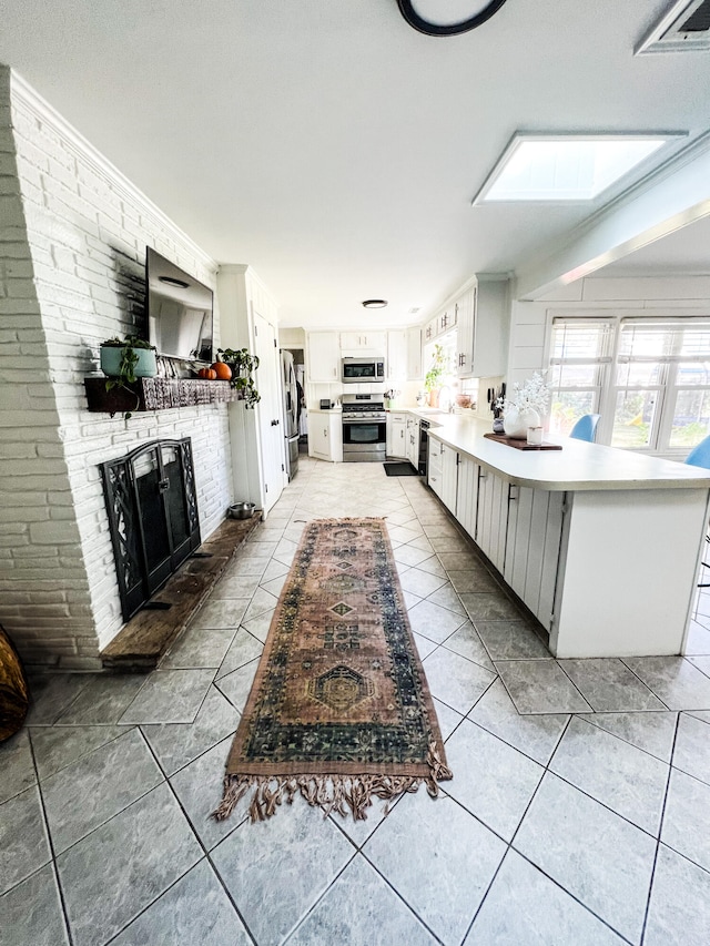 kitchen featuring kitchen peninsula, a skylight, stainless steel appliances, white cabinets, and light tile patterned flooring