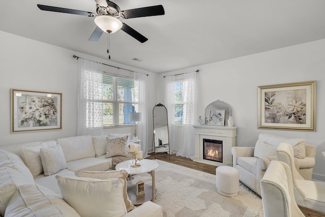 living room featuring a glass covered fireplace, ceiling fan, visible vents, and wood finished floors