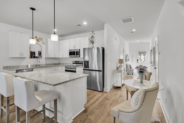 kitchen with visible vents, a kitchen island, white cabinetry, stainless steel appliances, and light wood-style floors