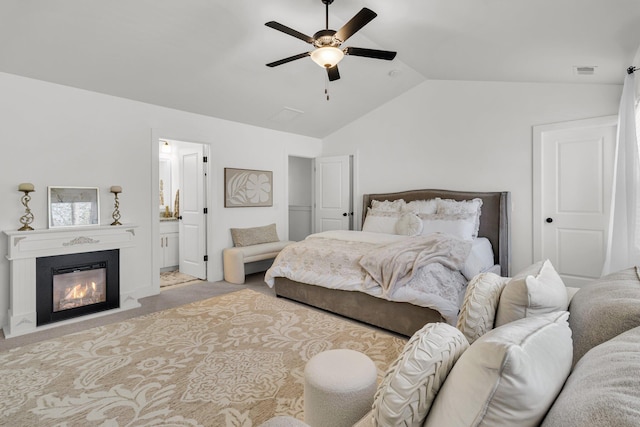 bedroom with visible vents, lofted ceiling, ensuite bath, a glass covered fireplace, and carpet flooring