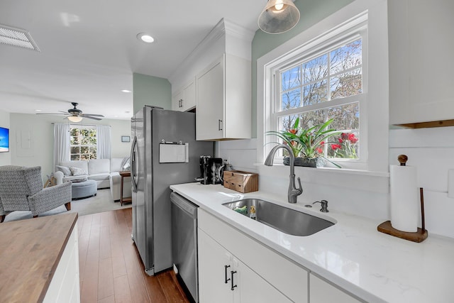 kitchen featuring visible vents, open floor plan, stainless steel dishwasher, white cabinetry, and a sink