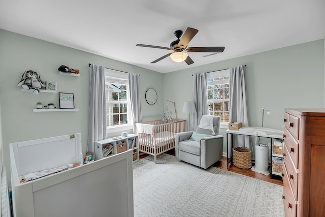 bedroom with a crib, wood finished floors, and a ceiling fan