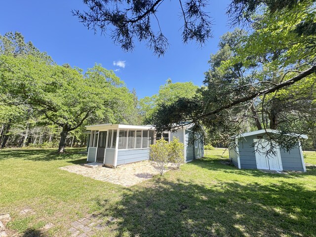 view of grassy yard with a sunroom, a shed, and an outbuilding