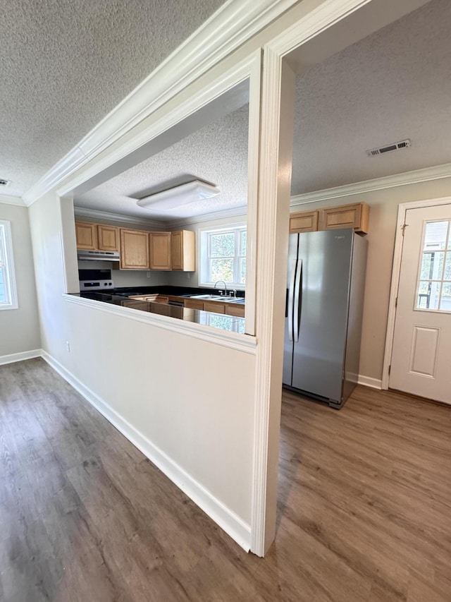 kitchen with a textured ceiling, stainless steel fridge, ornamental molding, wood finished floors, and plenty of natural light
