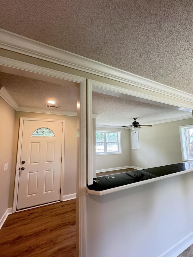 foyer entrance featuring a textured ceiling, crown molding, dark wood-type flooring, baseboards, and ceiling fan