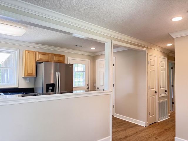 kitchen with stainless steel refrigerator with ice dispenser, crown molding, light wood-type flooring, tile counters, and recessed lighting