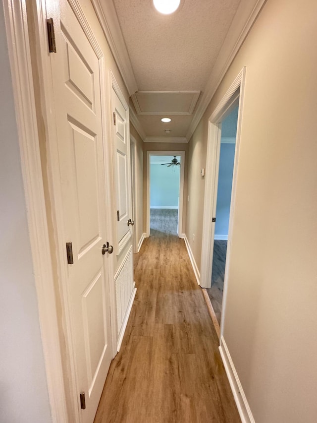 hallway featuring wood finished floors, baseboards, crown molding, and a textured ceiling