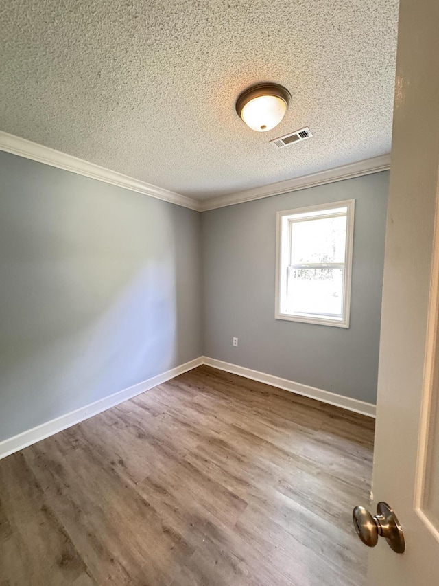 unfurnished room with a textured ceiling, ornamental molding, wood finished floors, and baseboards