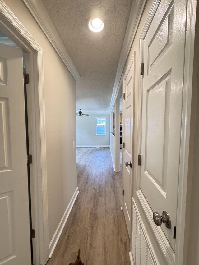 hallway featuring wood finished floors, a textured ceiling, baseboards, and crown molding