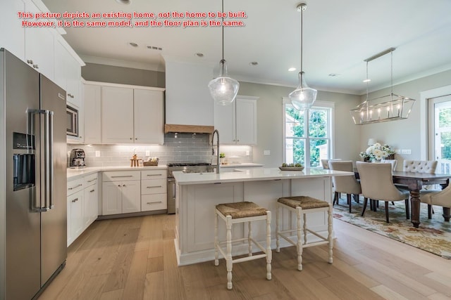 kitchen with white cabinets, decorative light fixtures, a center island with sink, and premium appliances