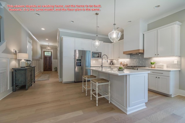 kitchen with white cabinetry, appliances with stainless steel finishes, premium range hood, and a kitchen island with sink