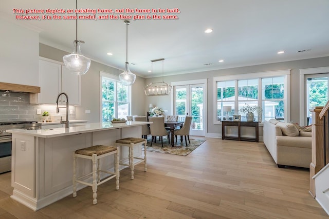 kitchen with gas range, a center island with sink, light wood-type flooring, decorative backsplash, and white cabinets