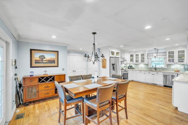 dining area with an inviting chandelier, light wood-type flooring, crown molding, and sink