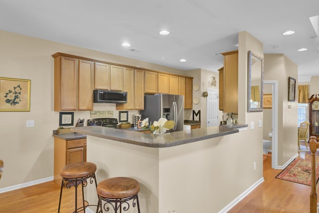 kitchen with kitchen peninsula, stainless steel appliances, light hardwood / wood-style floors, a kitchen bar, and light brown cabinets