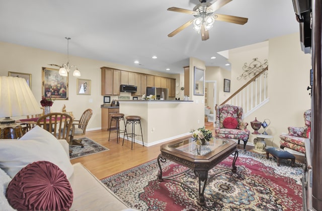 living room with ceiling fan with notable chandelier and light hardwood / wood-style floors