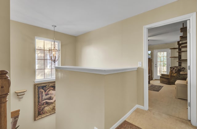 hallway featuring a chandelier and light carpet