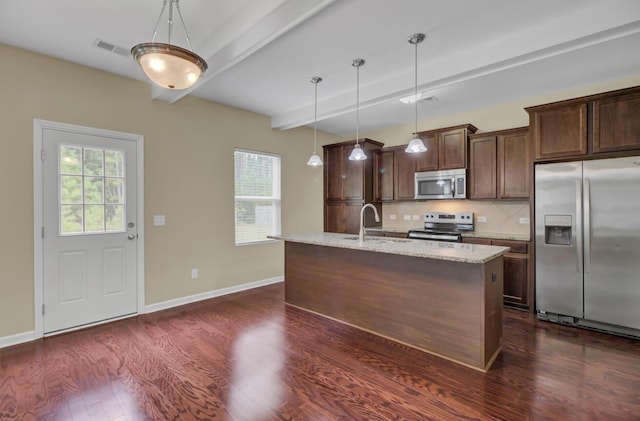 kitchen featuring hanging light fixtures, stainless steel appliances, light stone counters, beamed ceiling, and a kitchen island with sink