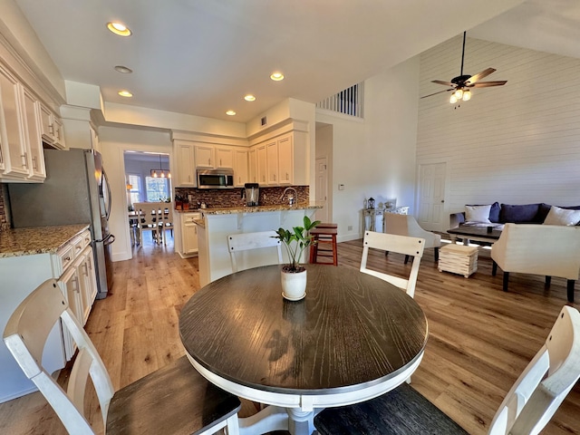 dining space with high vaulted ceiling, sink, and light hardwood / wood-style flooring