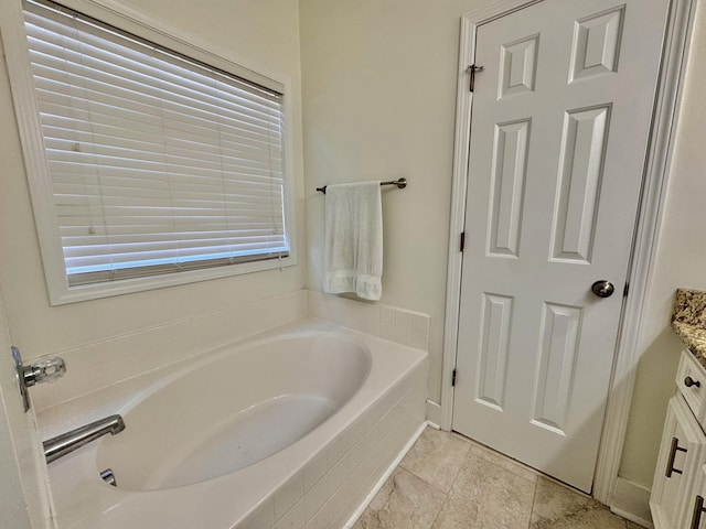 bathroom with tiled bath, vanity, and a healthy amount of sunlight