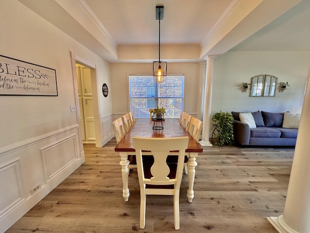 dining area with light wood-type flooring, a raised ceiling, and ornate columns