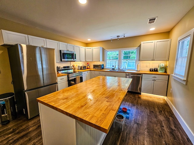 kitchen with appliances with stainless steel finishes, dark hardwood / wood-style flooring, wood counters, and white cabinets