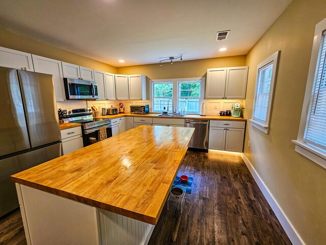 kitchen with stainless steel appliances, wood counters, white cabinets, sink, and dark hardwood / wood-style flooring