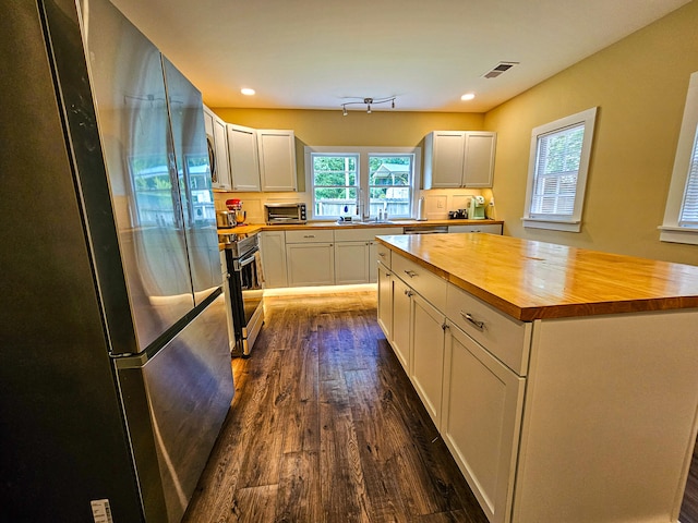 kitchen with butcher block counters, white cabinets, a kitchen island, dark hardwood / wood-style floors, and appliances with stainless steel finishes