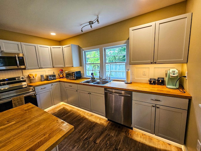 kitchen with butcher block countertops, appliances with stainless steel finishes, track lighting, sink, and dark hardwood / wood-style flooring