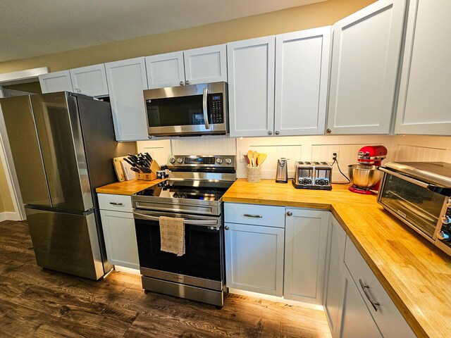 kitchen featuring appliances with stainless steel finishes, dark hardwood / wood-style flooring, and wood counters