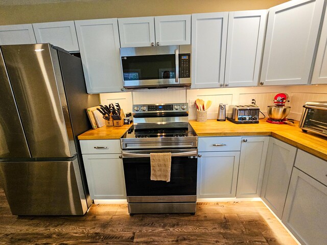 kitchen with appliances with stainless steel finishes, hardwood / wood-style flooring, white cabinets, and butcher block counters