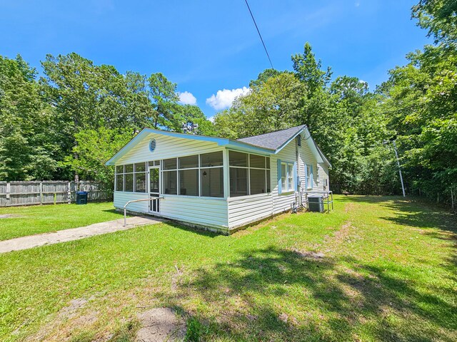 rear view of house with a sunroom, central AC, and a lawn