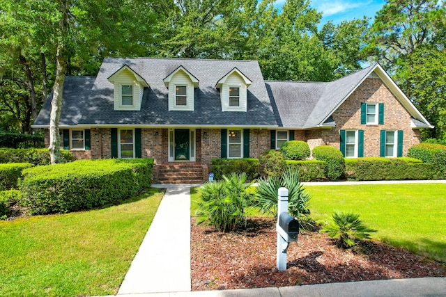 cape cod home featuring a shingled roof, a front lawn, and brick siding